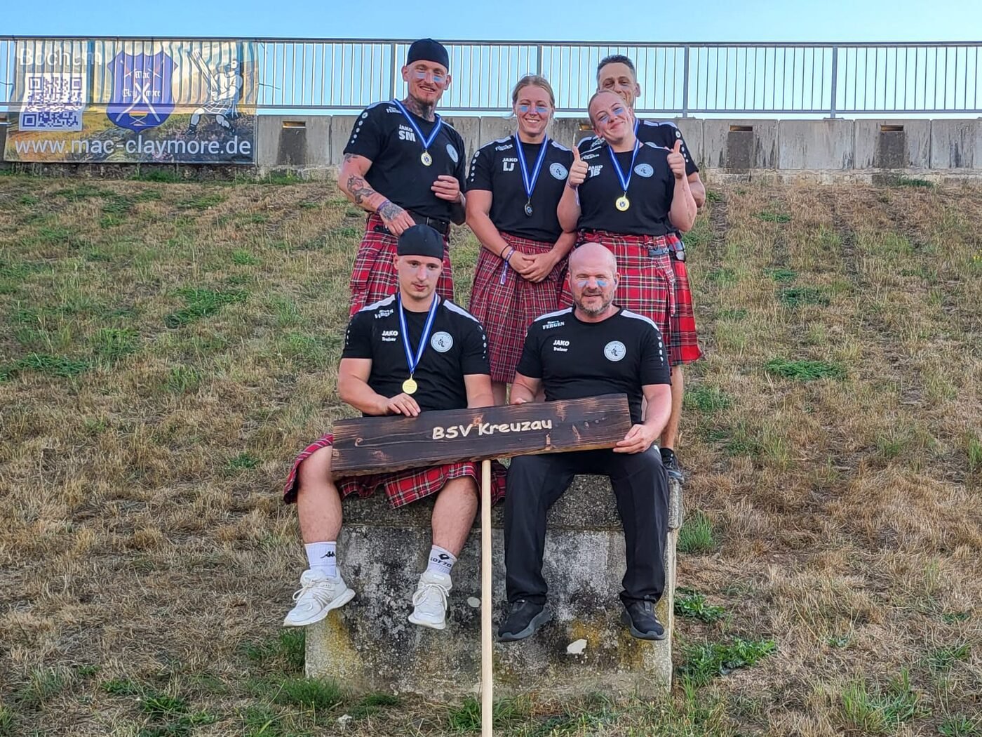 Sportlerinnen und Sportler des BSV Kreuzau mit Medaillen nach dem Wettkampf, davor das hölzerne Vereinsschild